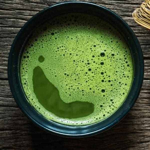 Close-up of a bowl of vibrant green matcha tea with foam, on a rustic wooden surface.