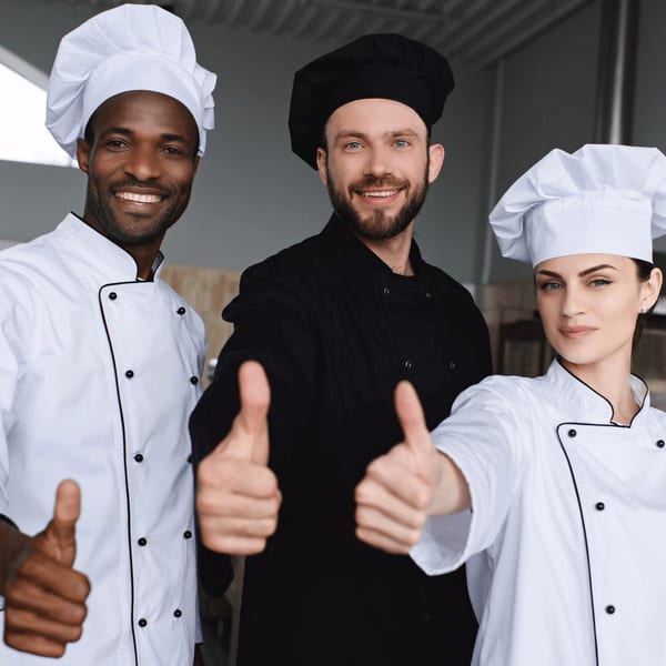 Three smiling EVOO Mediterranean Cuisine chefs, two men and one woman, give thumbs up to the camera.