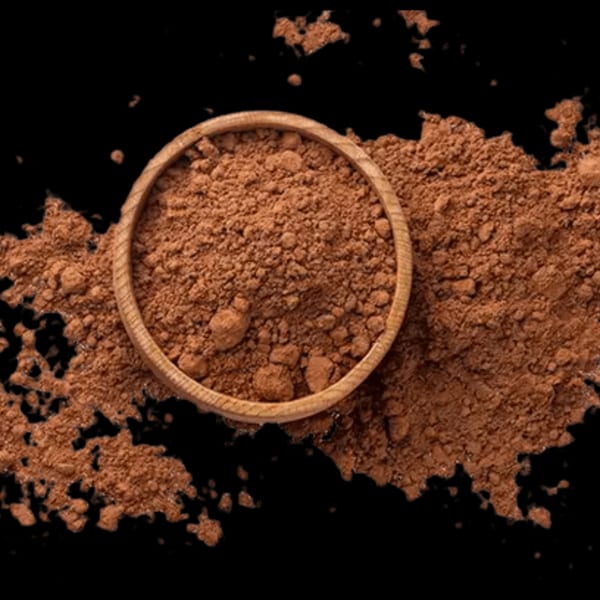 A wooden bowl filled with brown cocoa powder, with more powder scattered around it on a black surface.