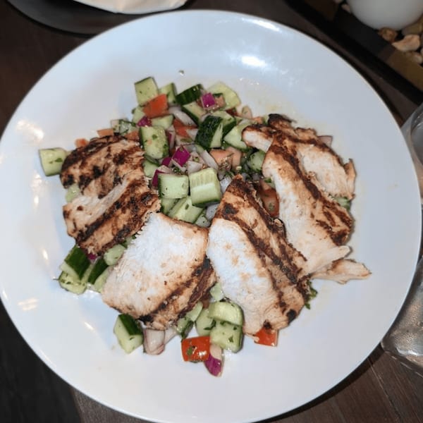 Grilled chicken slices over a fresh Mediterranean salad with cucumbers, tomatoes, and red onions.