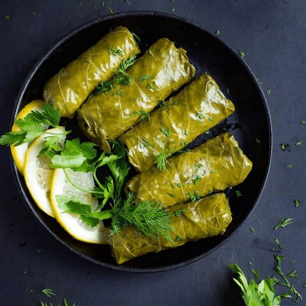 EVOO Mediterranean Cuisine's dolmades, grape leaves stuffed with rice, garnished with lemon slices and fresh herbs.