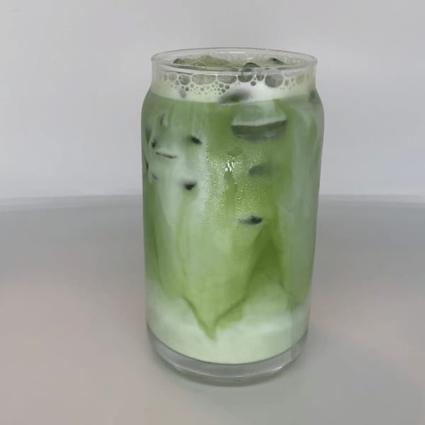 Iced matcha latte in a glass, with green tea swirling into white milk.