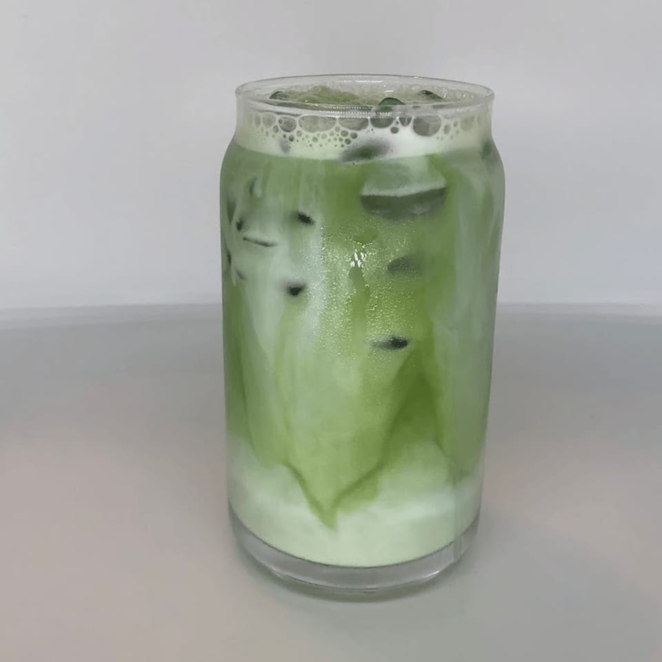 Iced matcha latte in a glass, with green tea swirling into white milk.