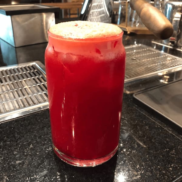 A vibrant red Mediterranean drink with a foamy top, in a clear glass on a dark counter.