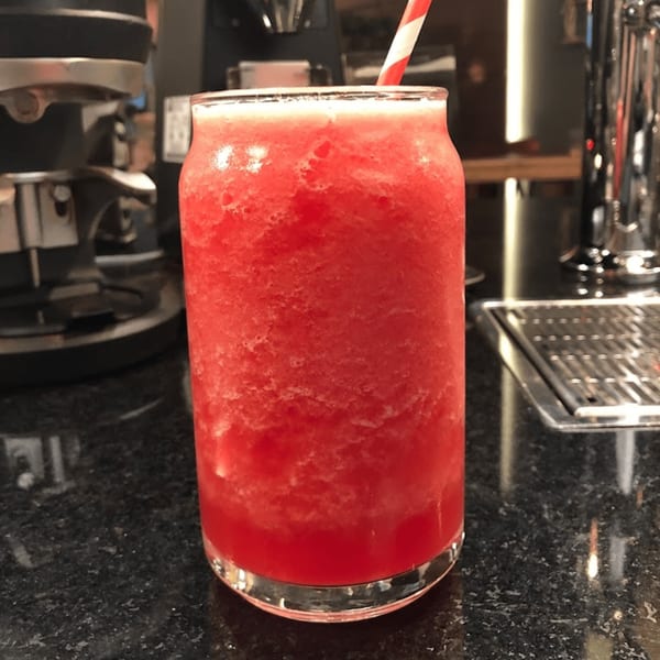 A vibrant red frozen drink with a striped straw sits on a dark speckled counter.