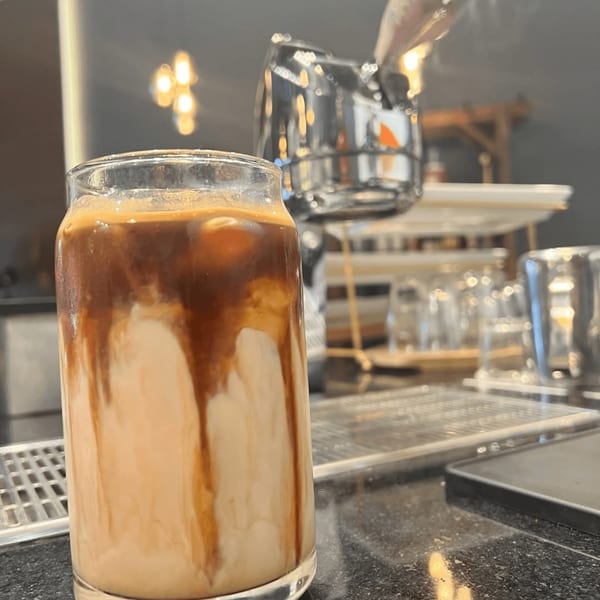 An iced coffee with milk and espresso swirls in a clear glass on a dark counter.