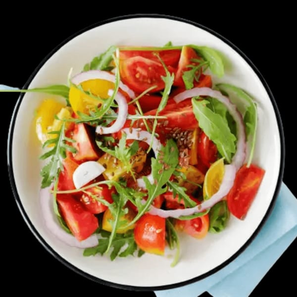 Vibrant Mediterranean salad with red and yellow tomatoes, red onion, arugula, and flax seeds.